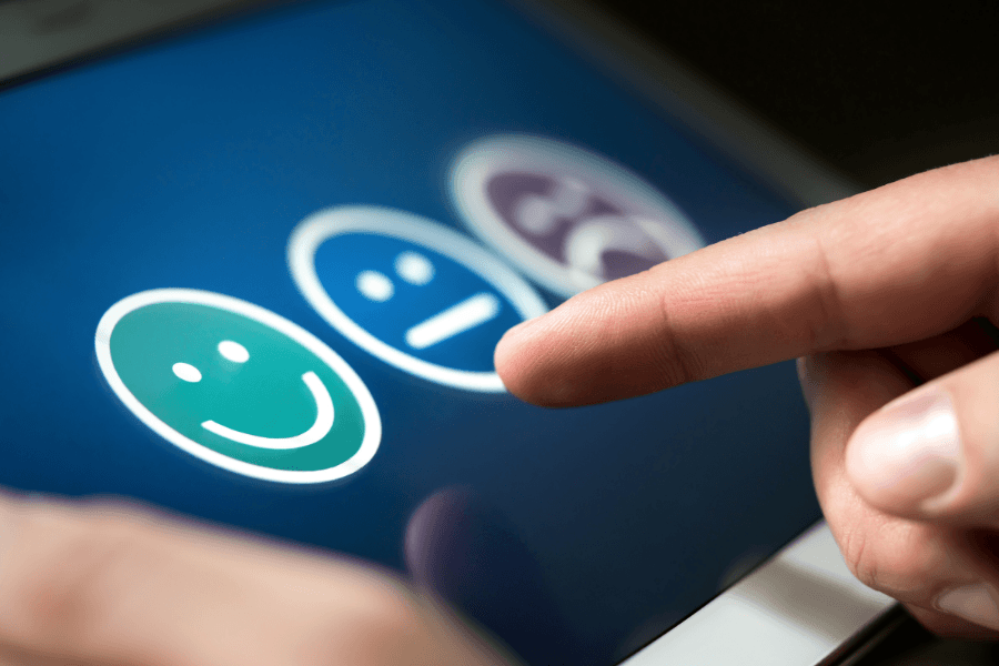 A close-up of a person's finger selecting a happy green smiley face icon on a digital tablet screen during a customer satisfaction survey.