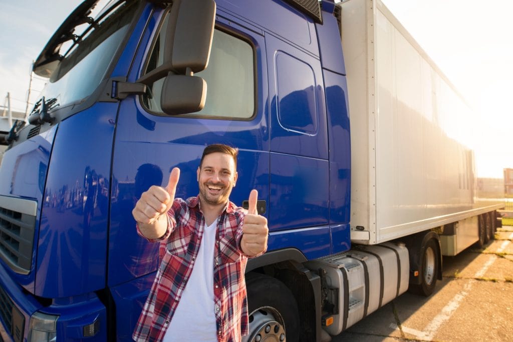 Satisfied truck driver giving thumbs up outside semi truck after using mono headset