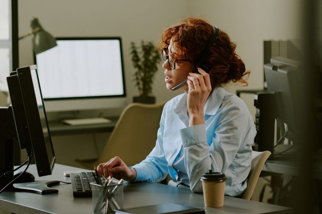 An office professional wearing a headset while typing on a computer at her desk