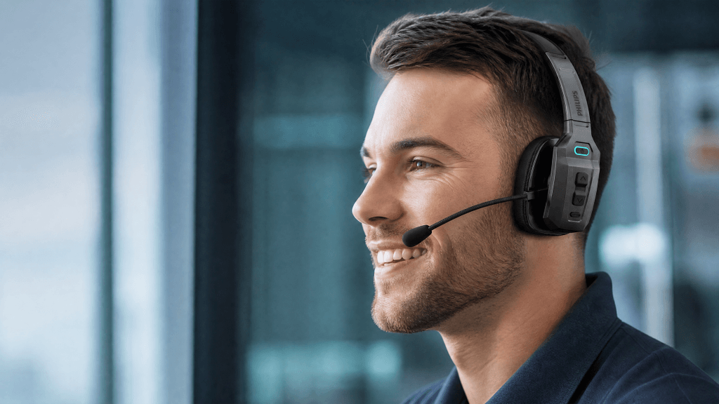 A professional man wearing the Philips TAL8000 mono headset while smiling near an office window.