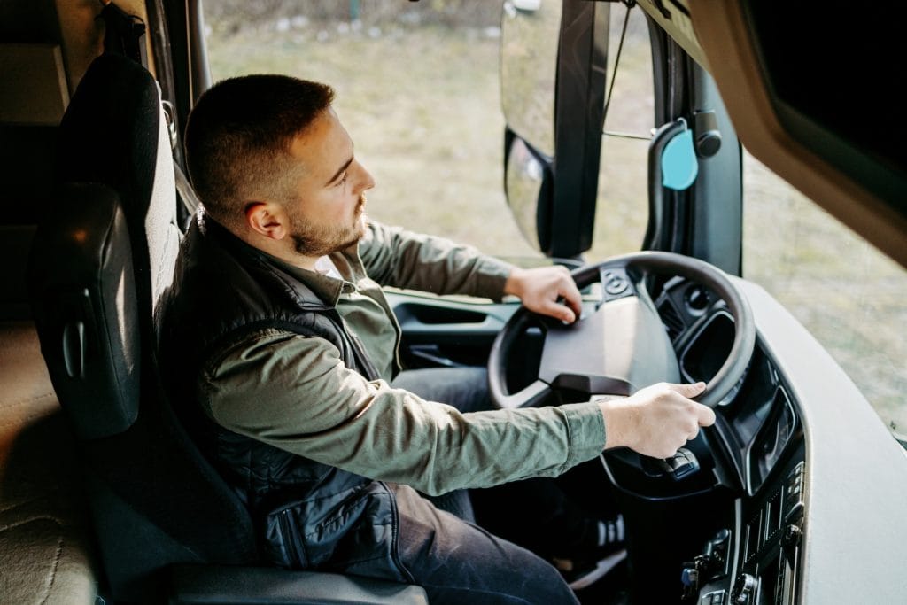 A professional truck driver focused on the road while gripping the steering wheel inside a semi-truck cab.