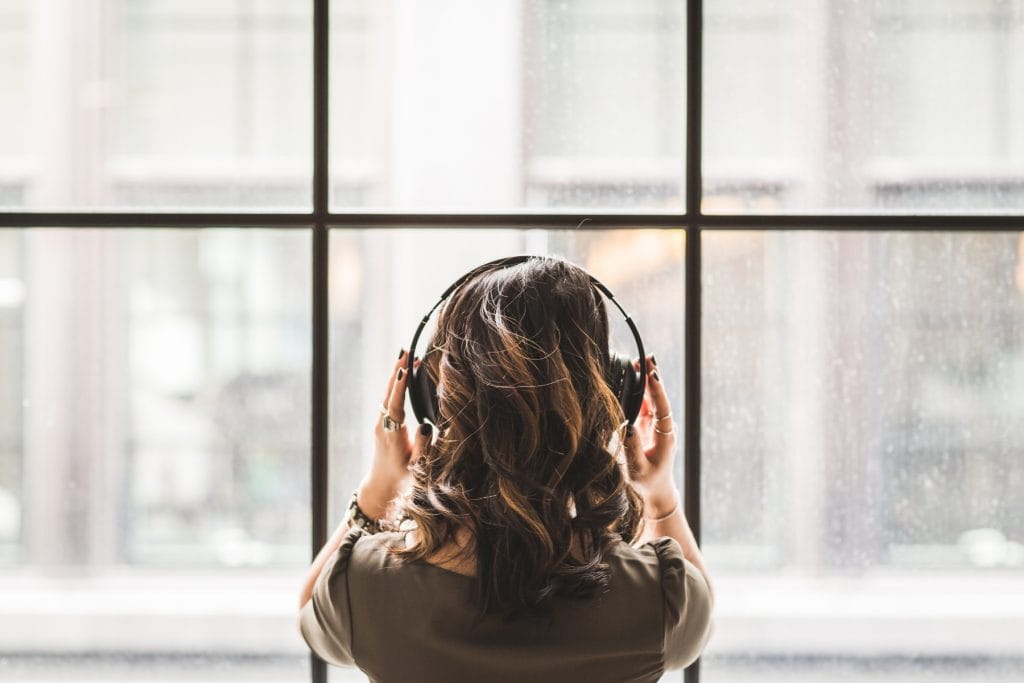 Woman wearing noise-canceling headphones looking out a window while listening intently in a quiet moment