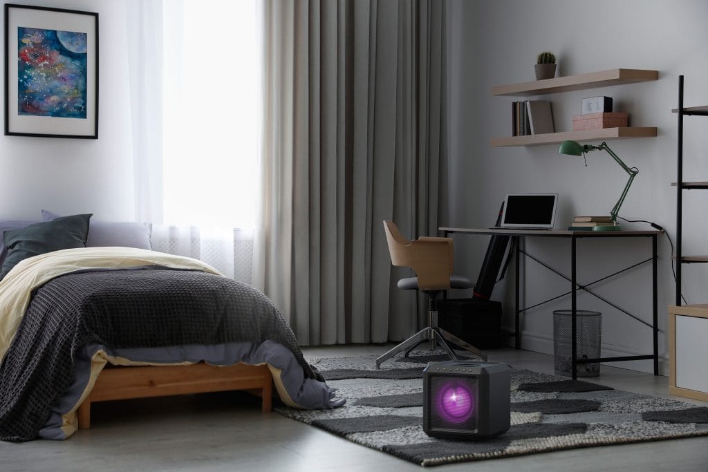 Philips cube speaker with ambient purple lighting placed on a bedroom floor near a desk