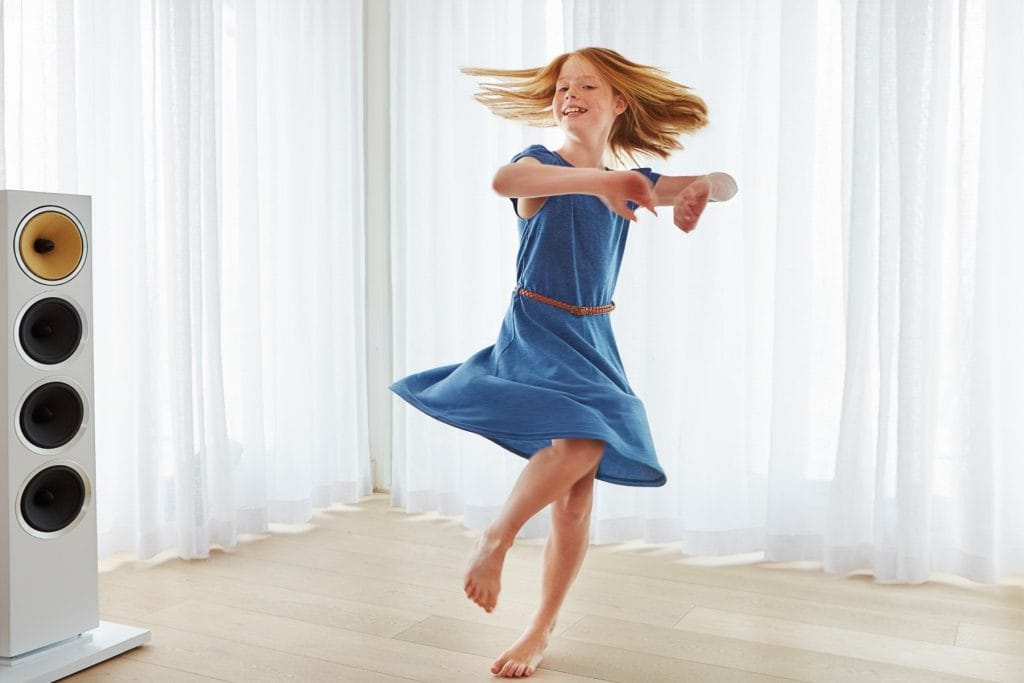Young girl dancing at home next to a floor-standing speaker showing dynamic lifestyle audio