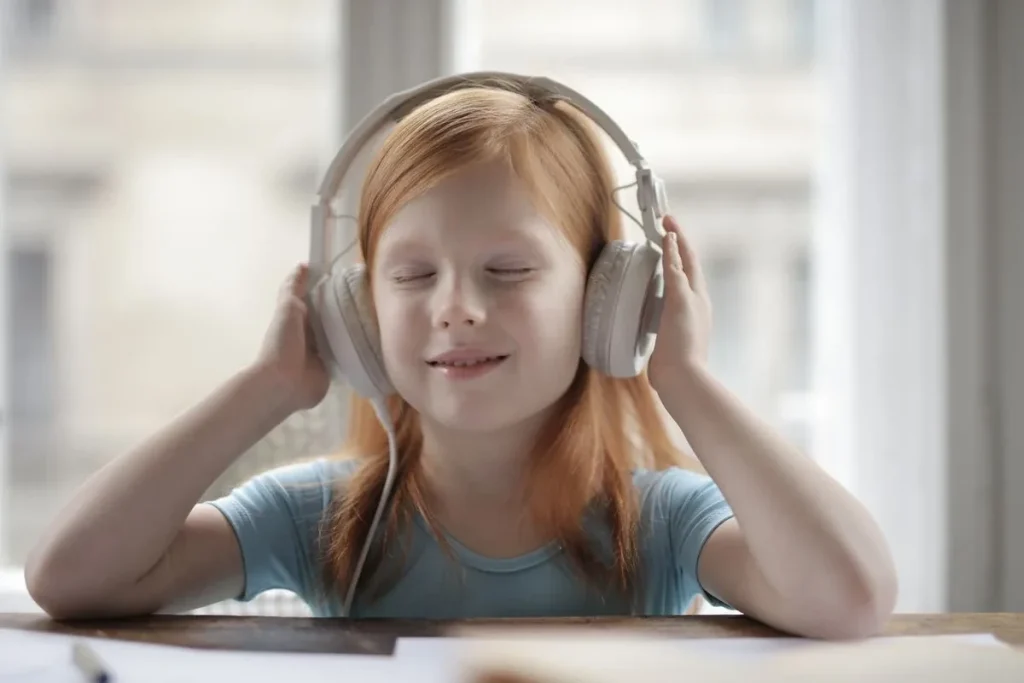 Girl wearing headphones at home with her hands resting on the ear cups.